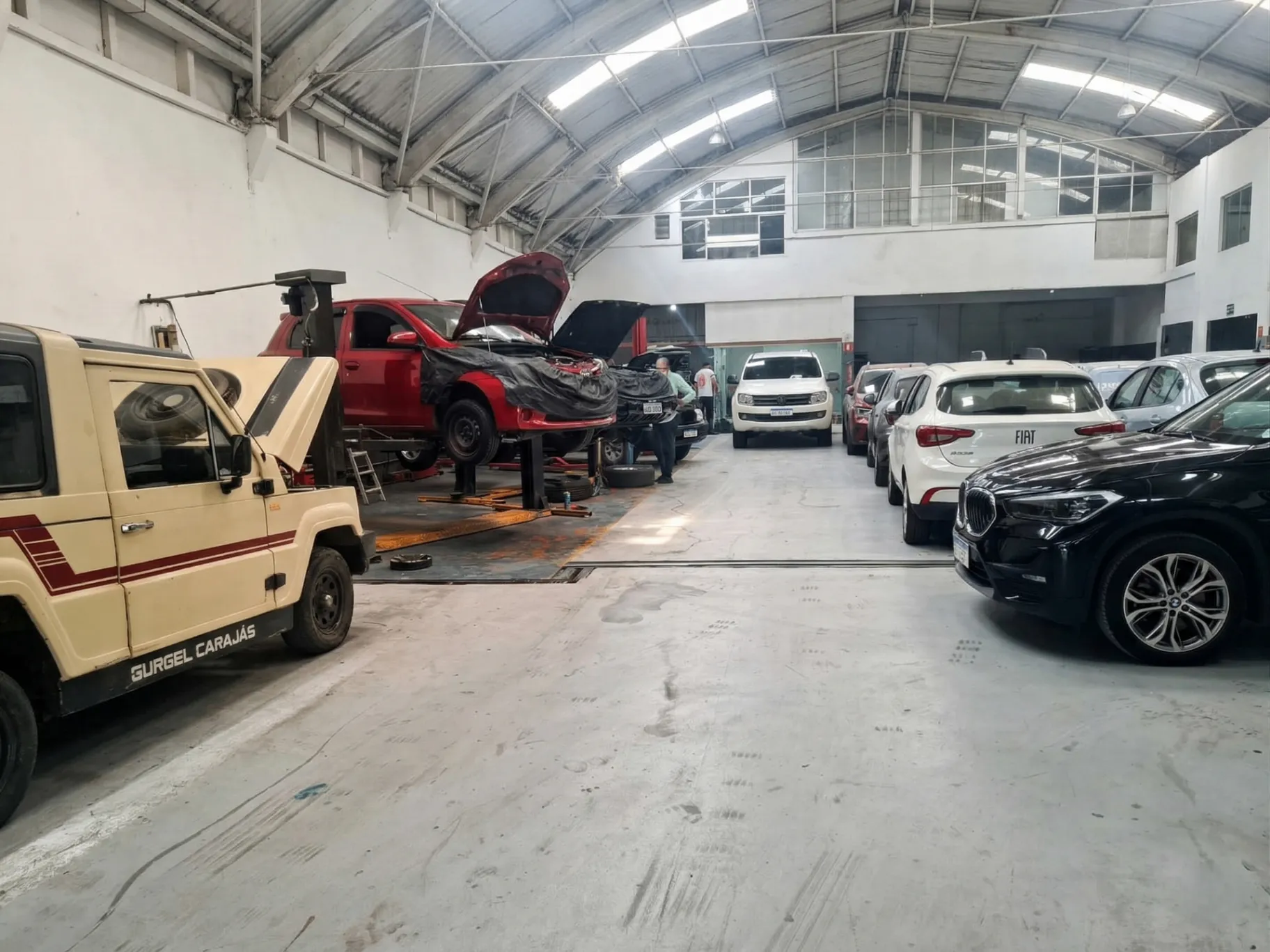 Galpão da oficina com veículos, elevador automotivo e equipe em atendimento.